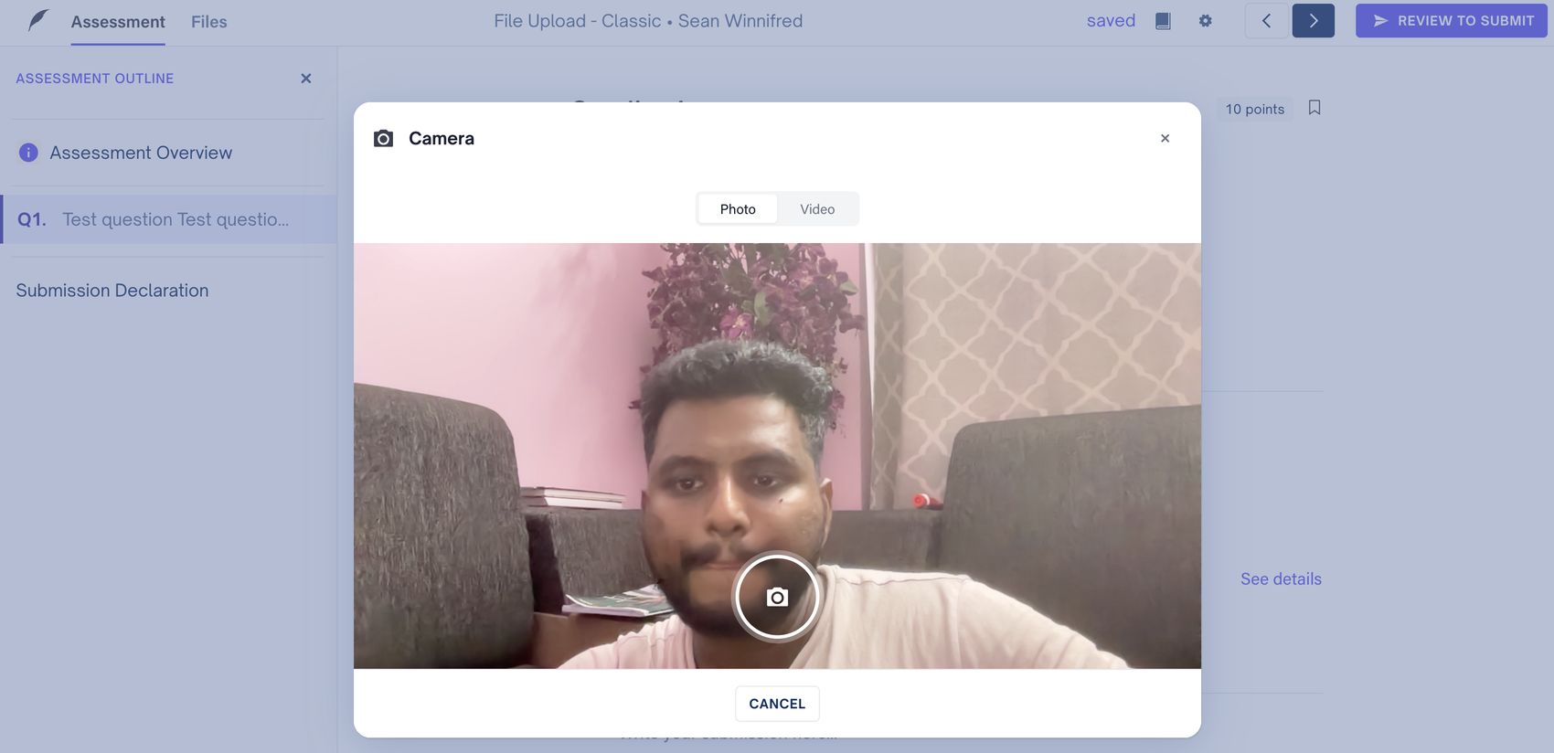 Camera modal open over a Cadmus assessment, showing photo and video tabs and a live webcam feed
